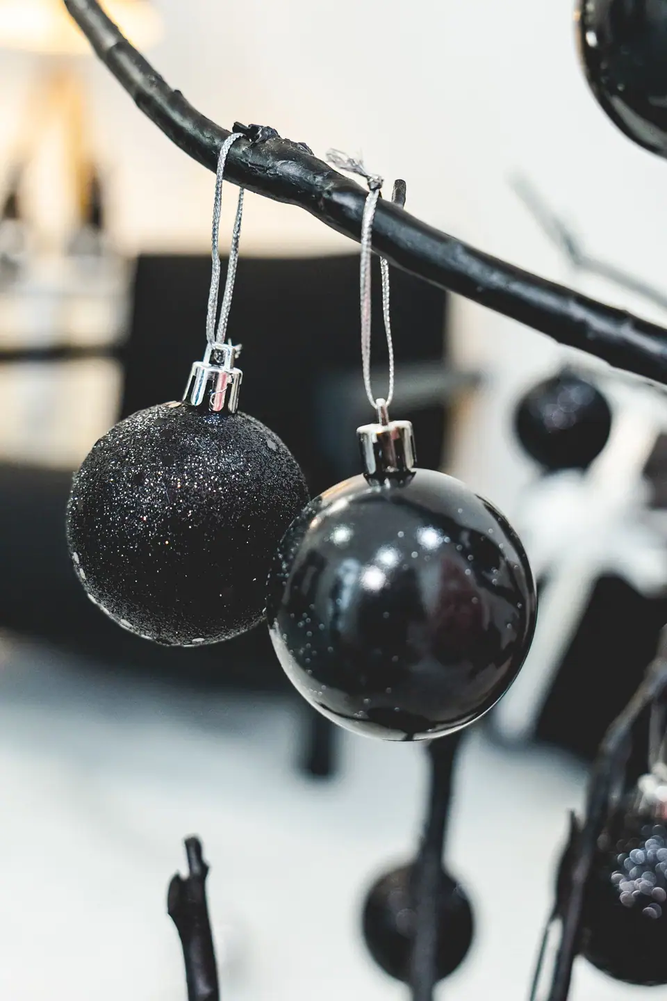 Two black Christmas ornaments, one glitter and one glossy, hanging from a black branch