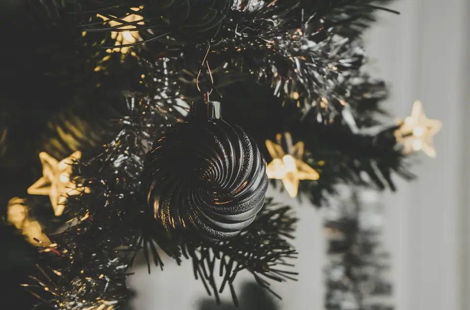 A black glass ornament with star lights on a dark Christmas tree