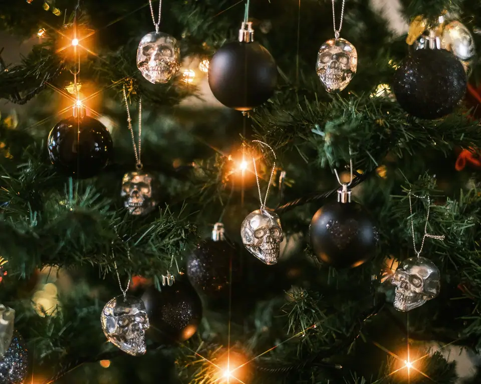 Silver skull ornaments and matte and glitter black balls hanging on a lit Christmas tree