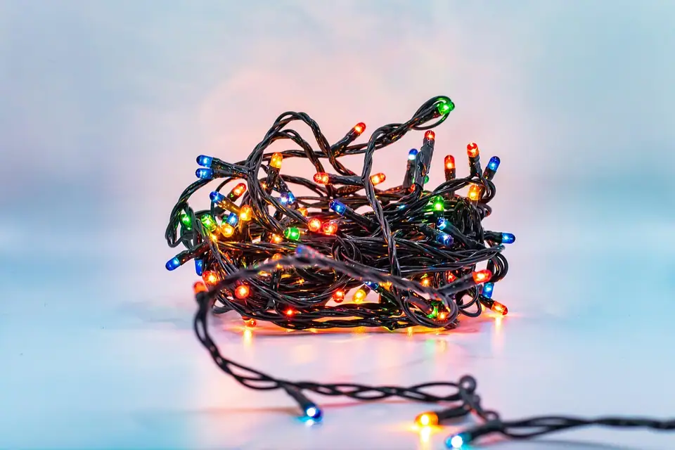 A tangle of multicolor mini Christmas lights on dark wire glowing against a pale background