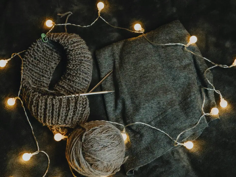 Gray knitted wool, a ball of yarn and a string of small lights on a dark blanket
