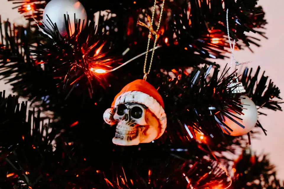 A skull ornament wearing a Santa hat on a black tinsel Christmas tree lit with orange lights
