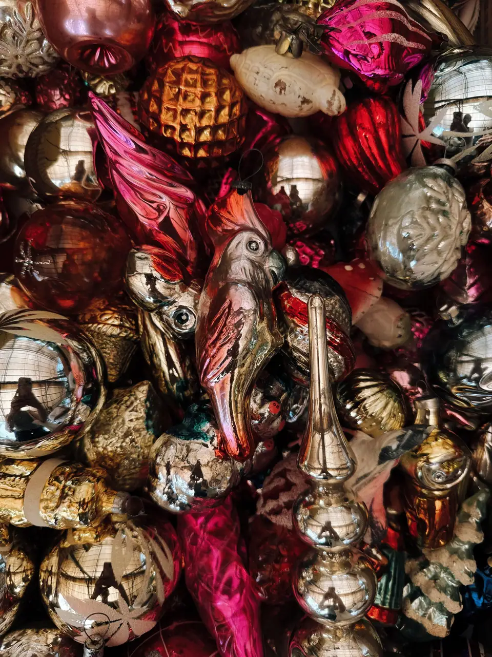 A heap of vintage glass Christmas ornaments shaped like birds and figures in silver, red and gold