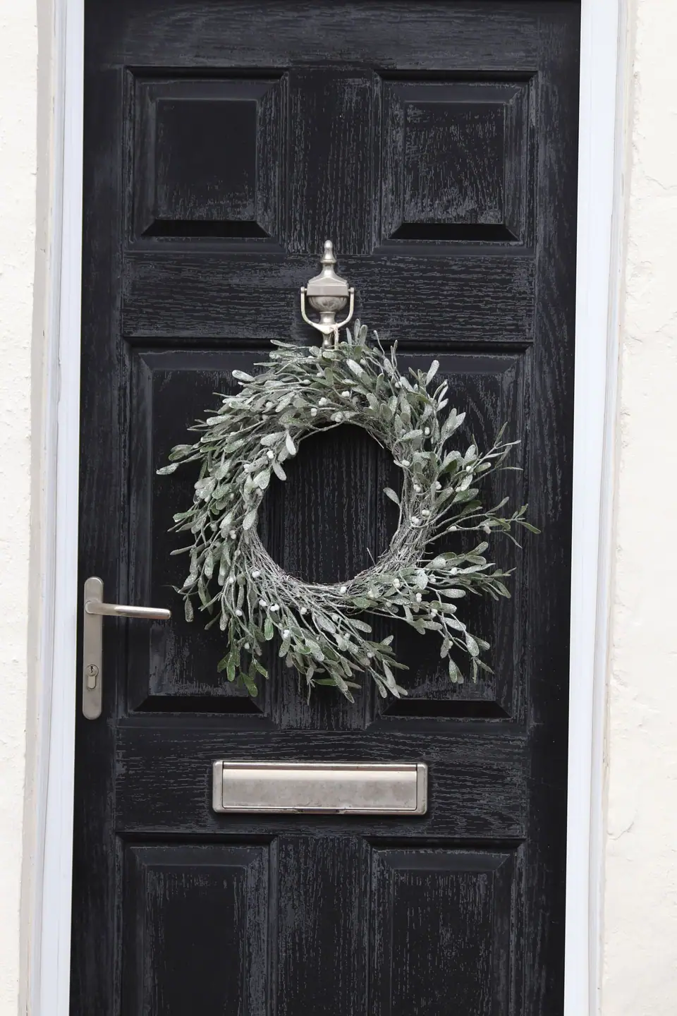 A frosted green winter wreath hanging on a black wooden front door